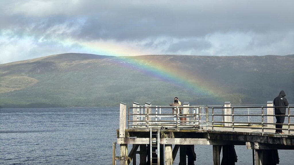 Rainbow over a loch with people standing on a wooden pier